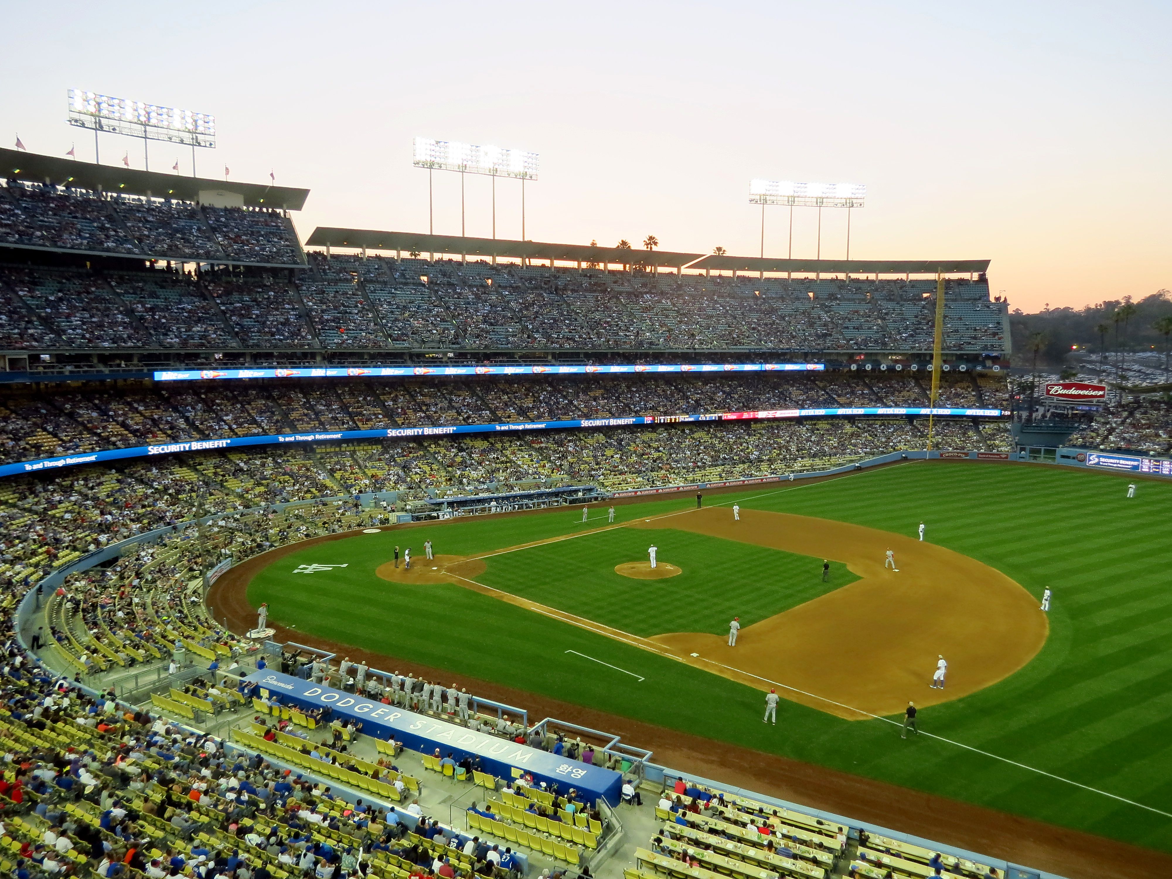 Aerial view of a packed baseball stadium at dusk with players on the field.