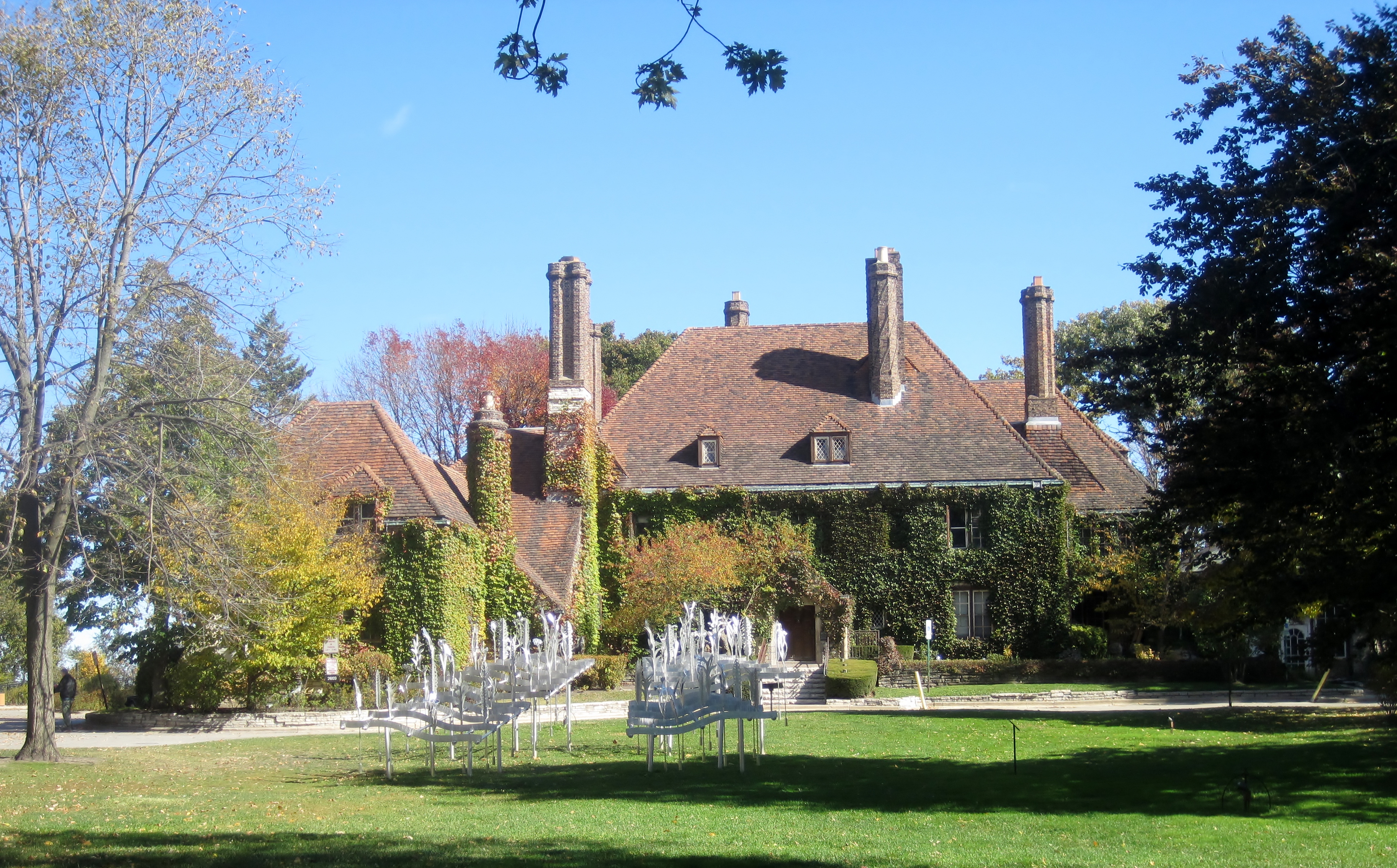 Large ivy-covered brick mansion with fountain sculptures on a manicured lawn.
