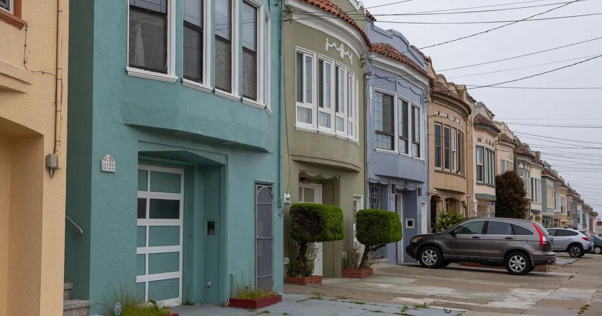 Colorful two-story attached homes lining a quiet residential street with parked cars.