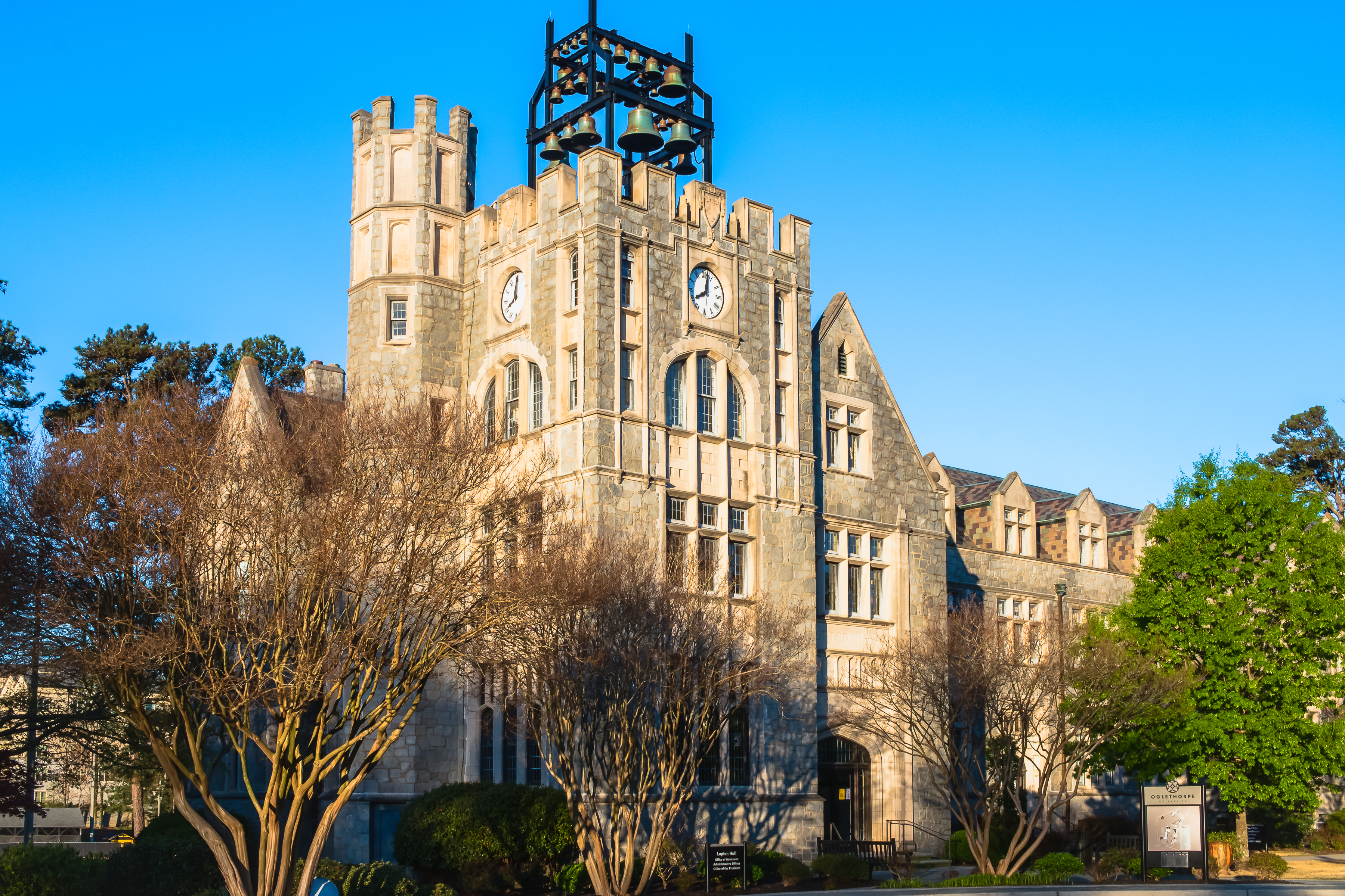 Gothic stone university building with a clock tower and crenellated turrets under a blue sky.