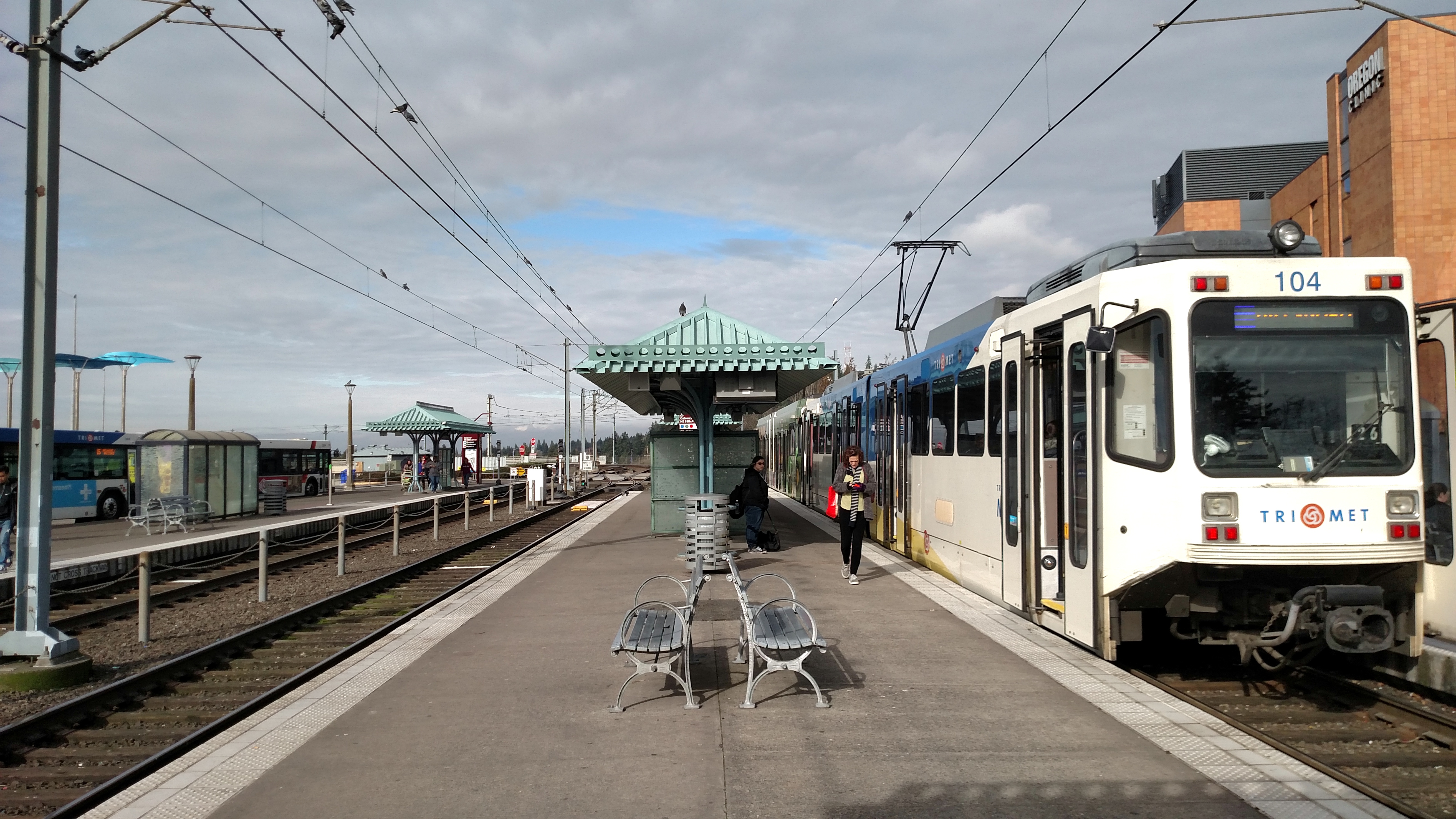 A TriMet MAX light rail train stopped at a covered transit center platform.