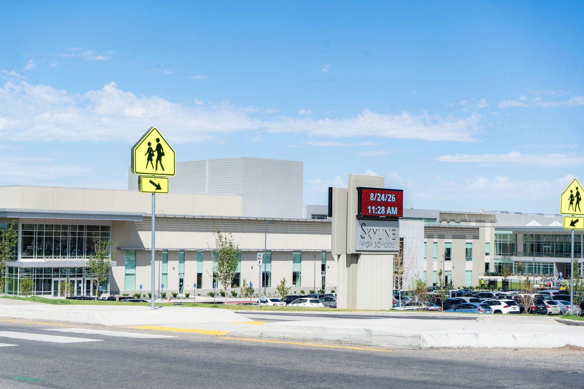 Modern high school building exterior with a roadside marquee and pedestrian crossing signs.