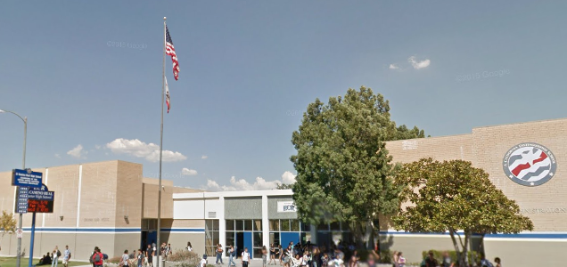 Brick school entrance with flagpoles, school seal, and blue marquee sign outside.