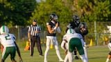 High school football players at the line of scrimmage during a game on a grass field.