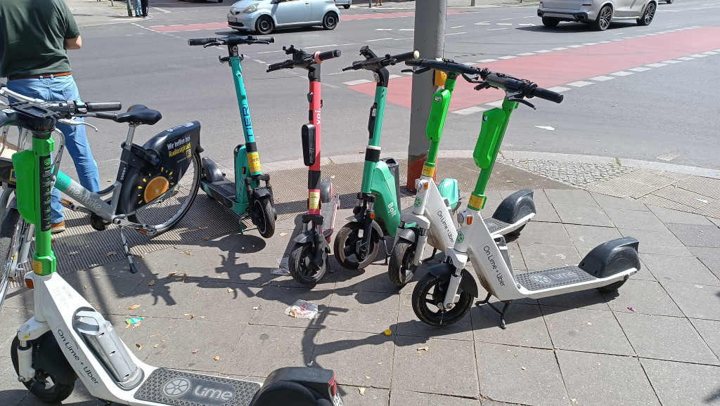 Electric scooters and an e-bike parked on a city sidewalk at a street corner.
