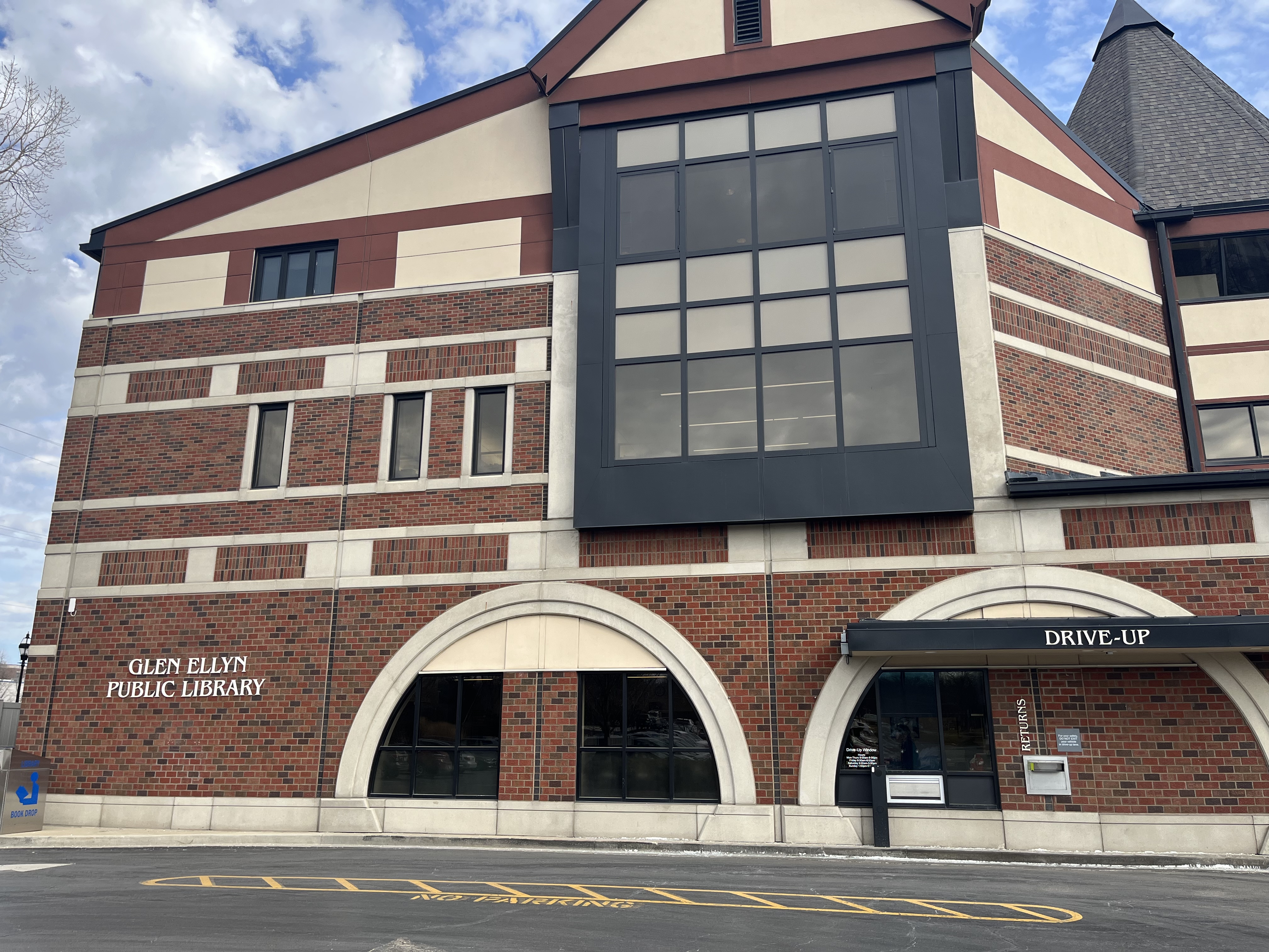 Brick library building exterior with arched windows and a drive-up window in winter.
