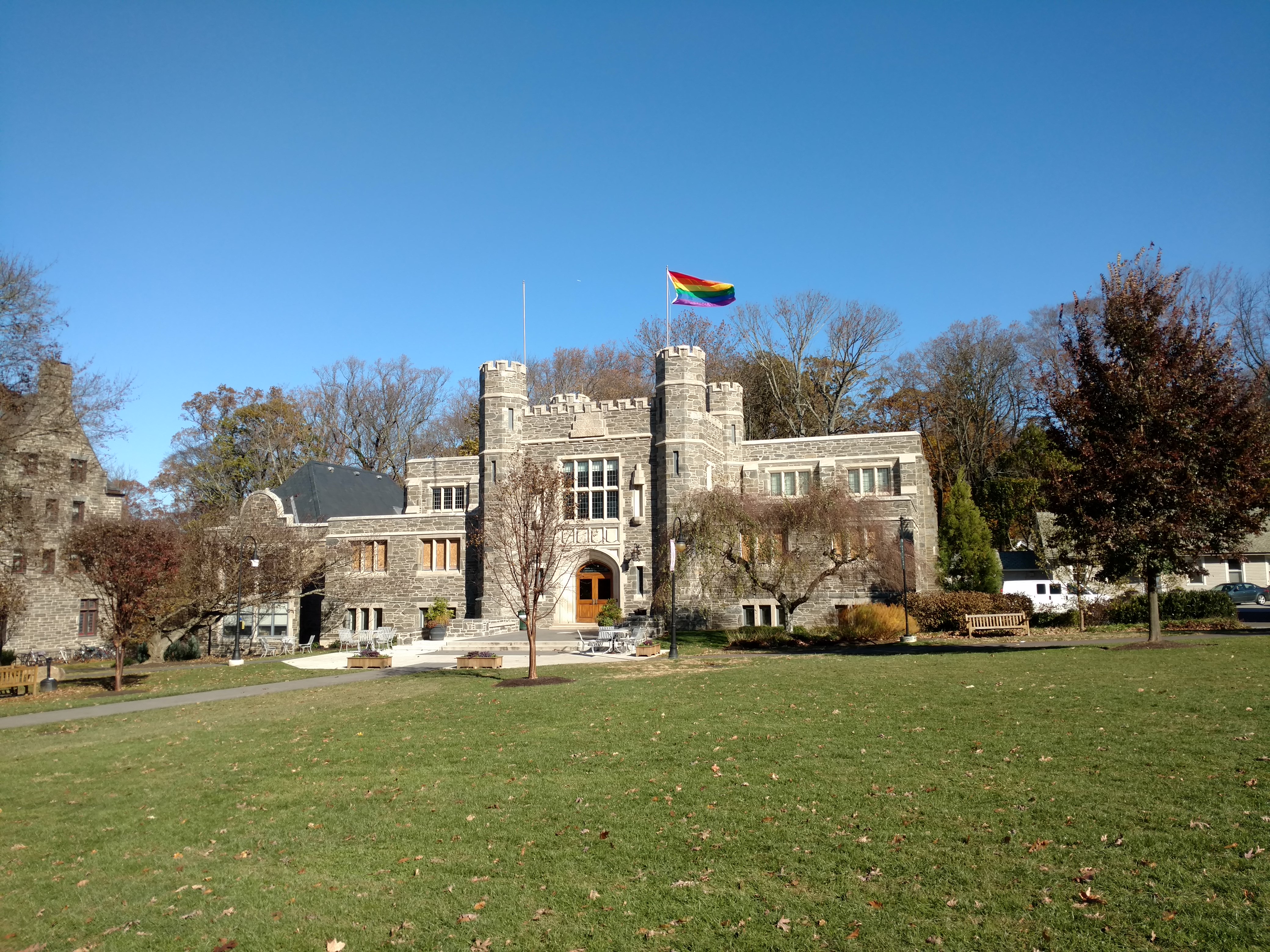 Gothic stone college building with a rainbow flag flying from its rooftop.
