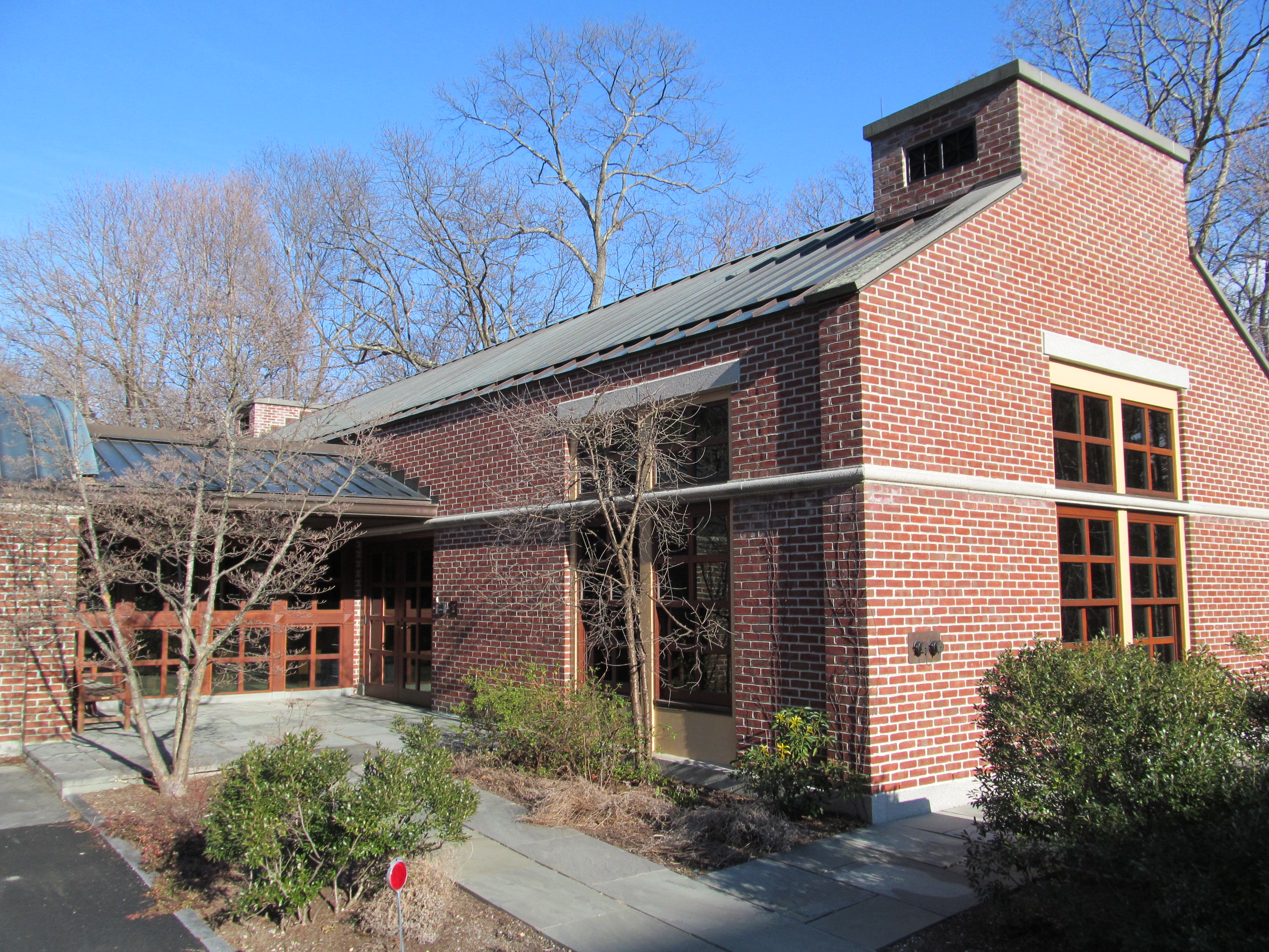 Red brick building with green metal roof and glass entryway surrounded by bare trees.