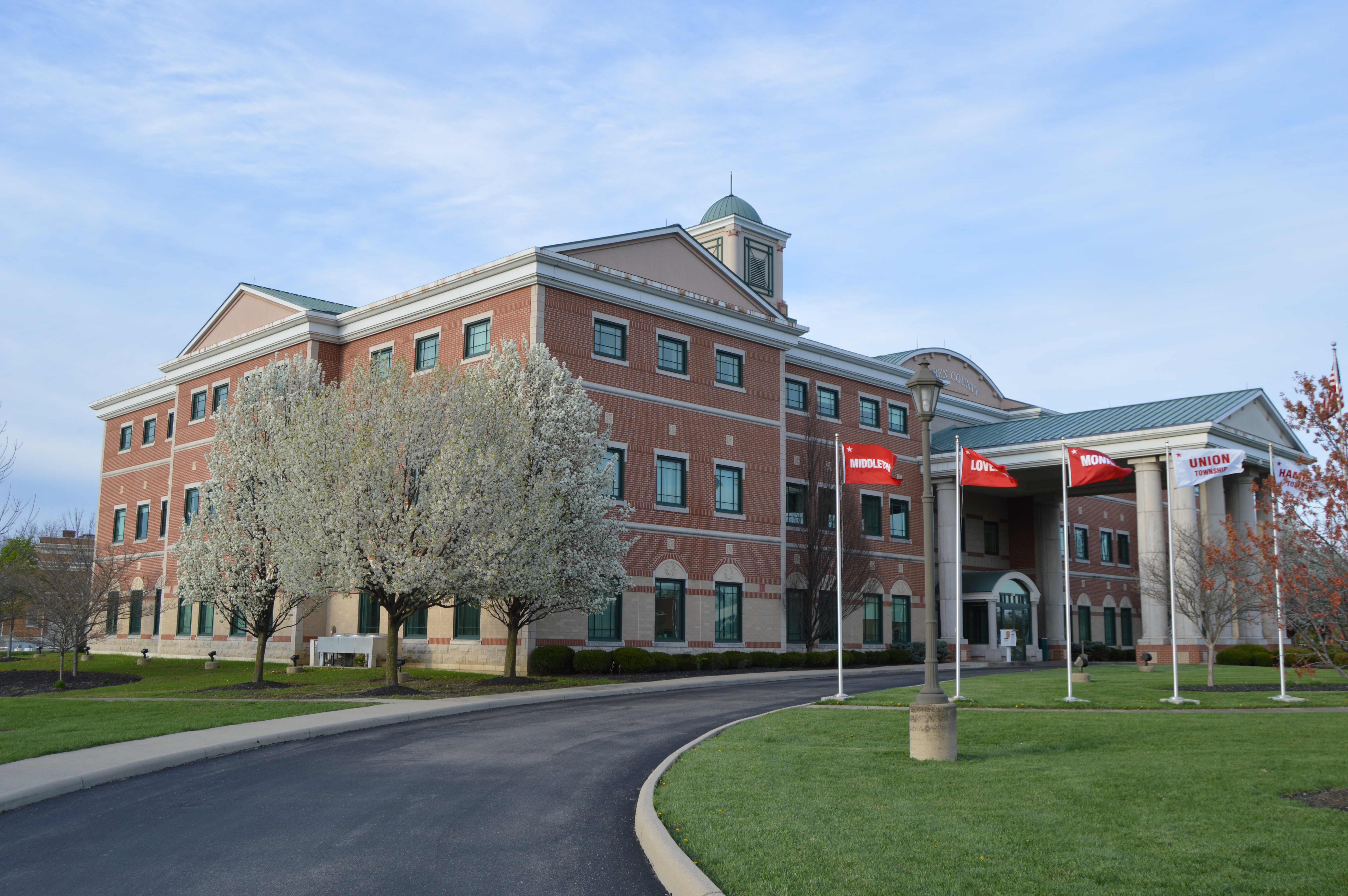 Red brick courthouse building with a cupola and flagpoles, surrounded by blooming trees.