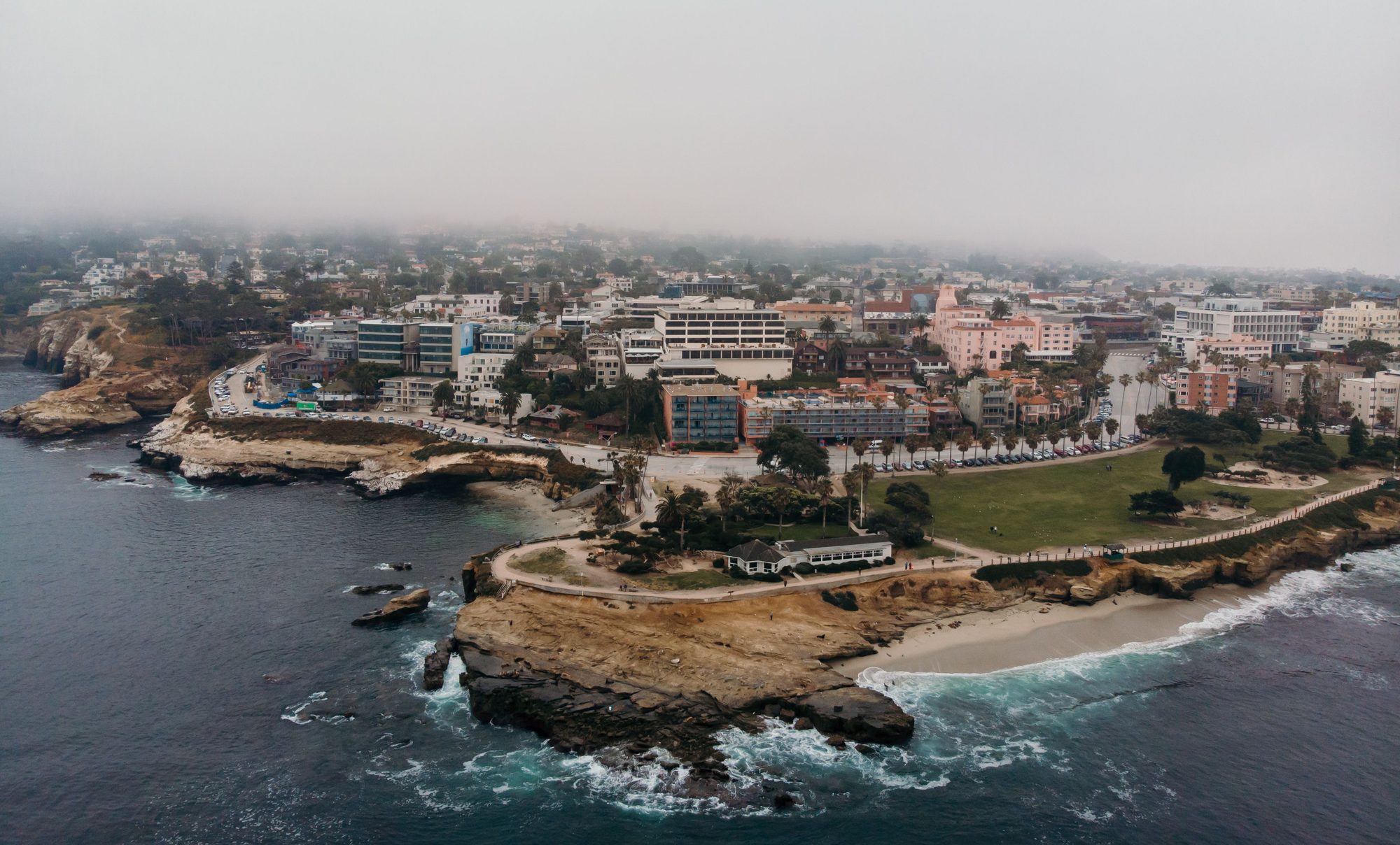 Aerial shot of La Jolla Cove in San Diego, California, showcasing coastal cliffs, cityscape, and foggy atmosphere.