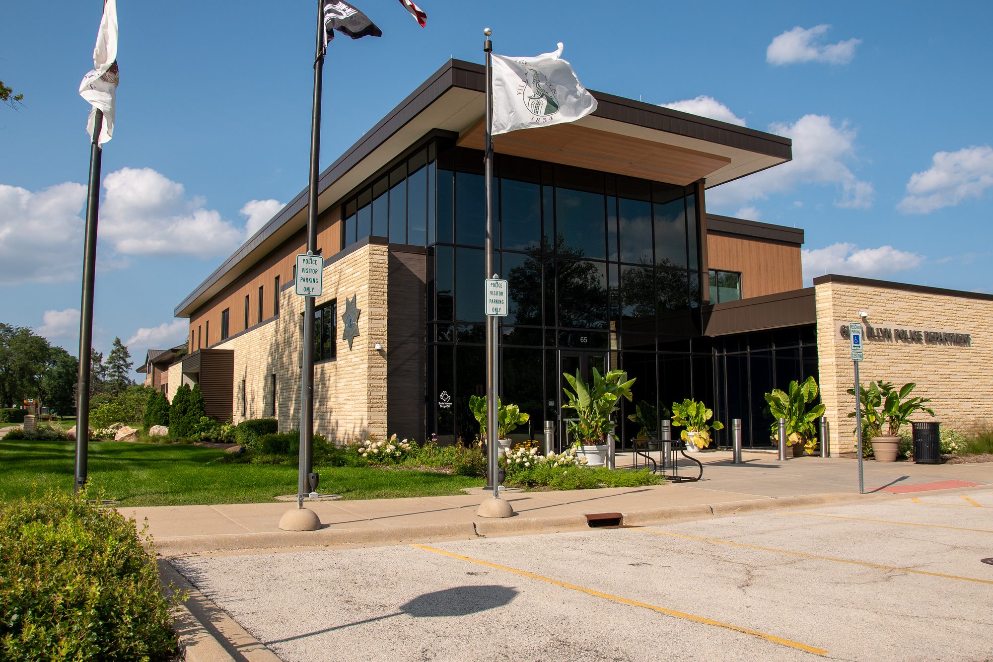 Modern two-story police department building with glass facade and three flagpoles.