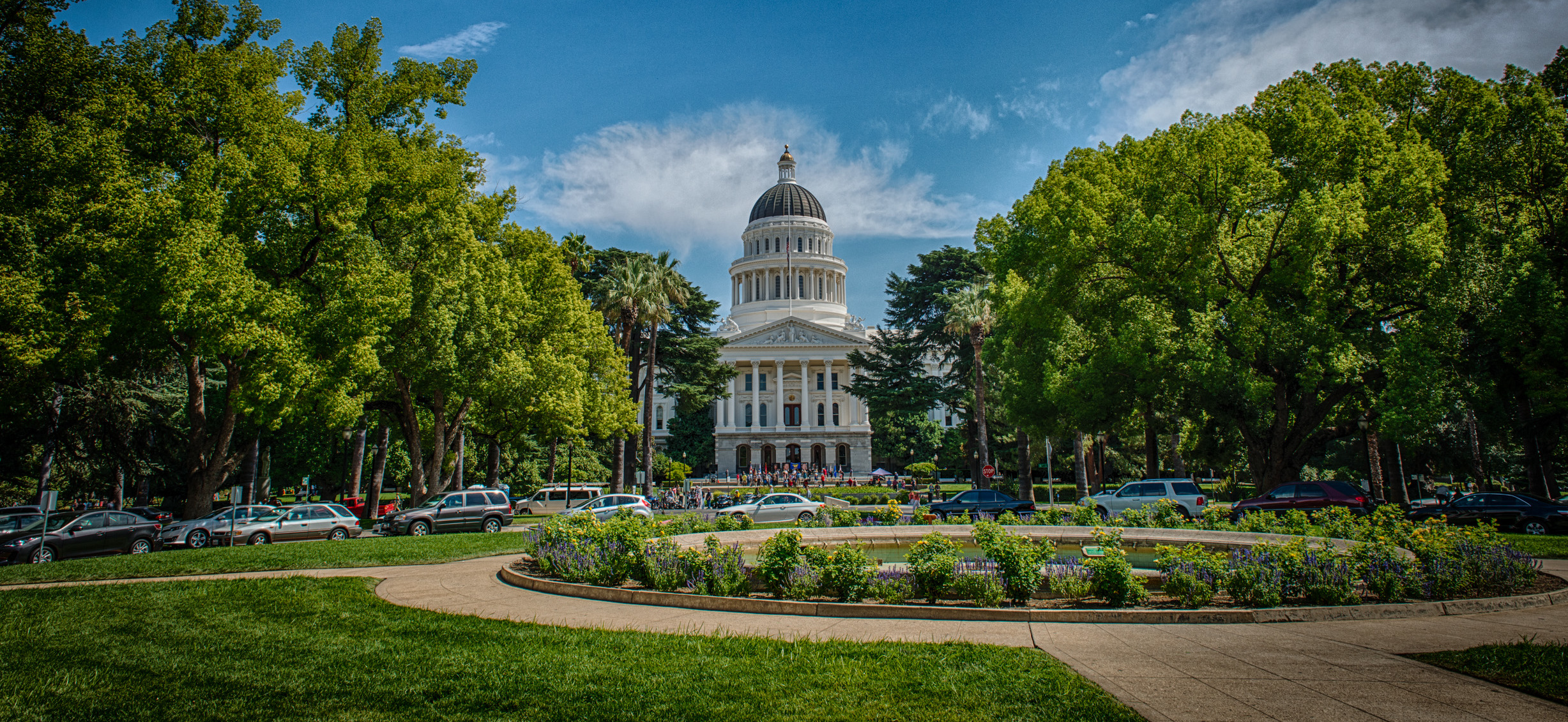 White-domed California State Capitol building seen through tree-lined park grounds.