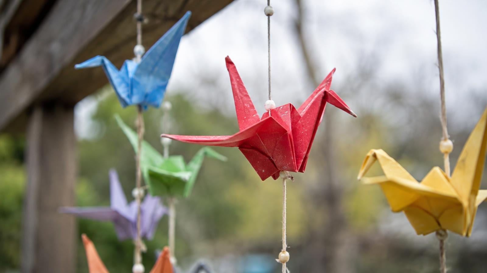 A string of colorful folded paper cranes hanging outdoors in soft light.