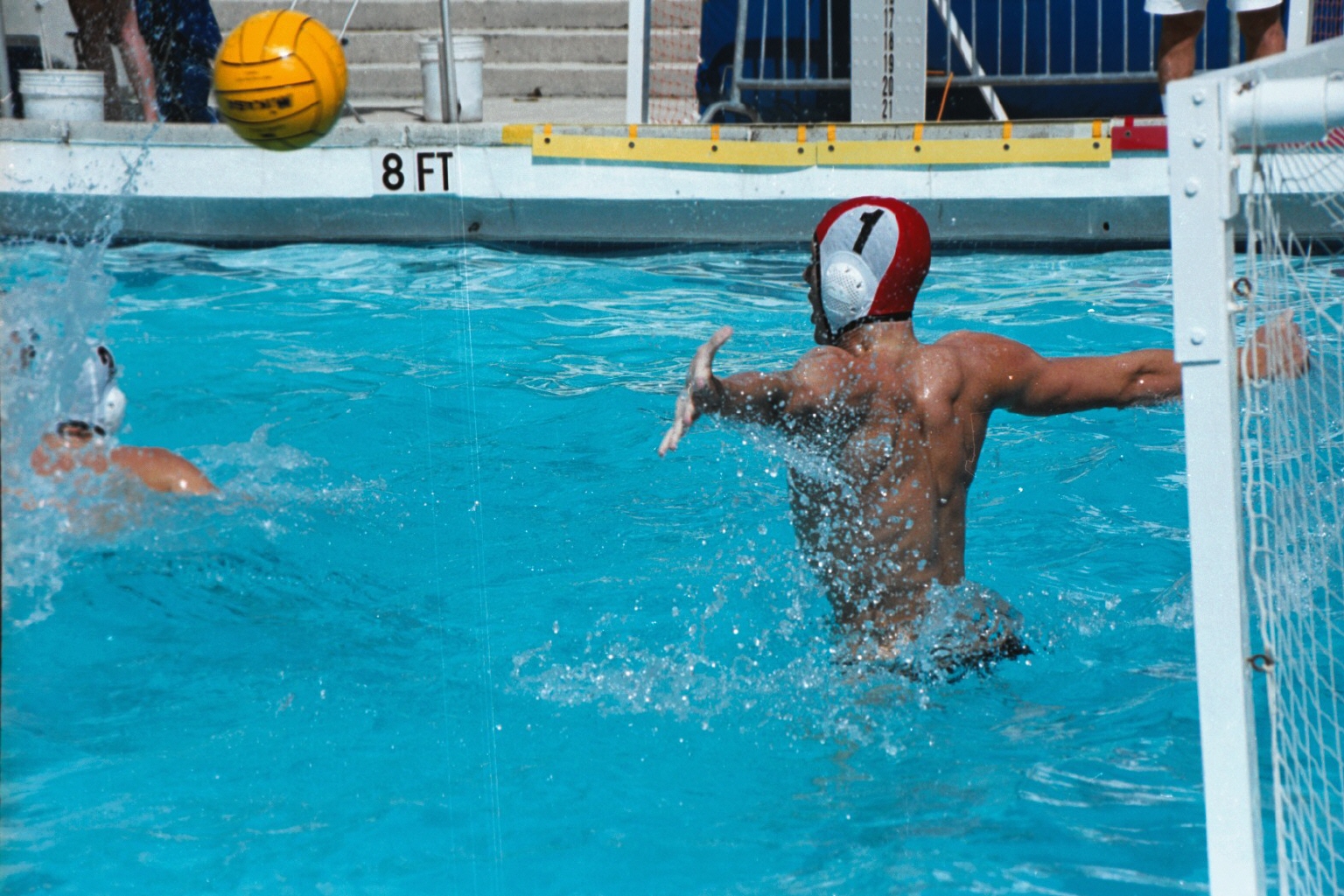 Two players compete near a goal during a water polo match in a pool.