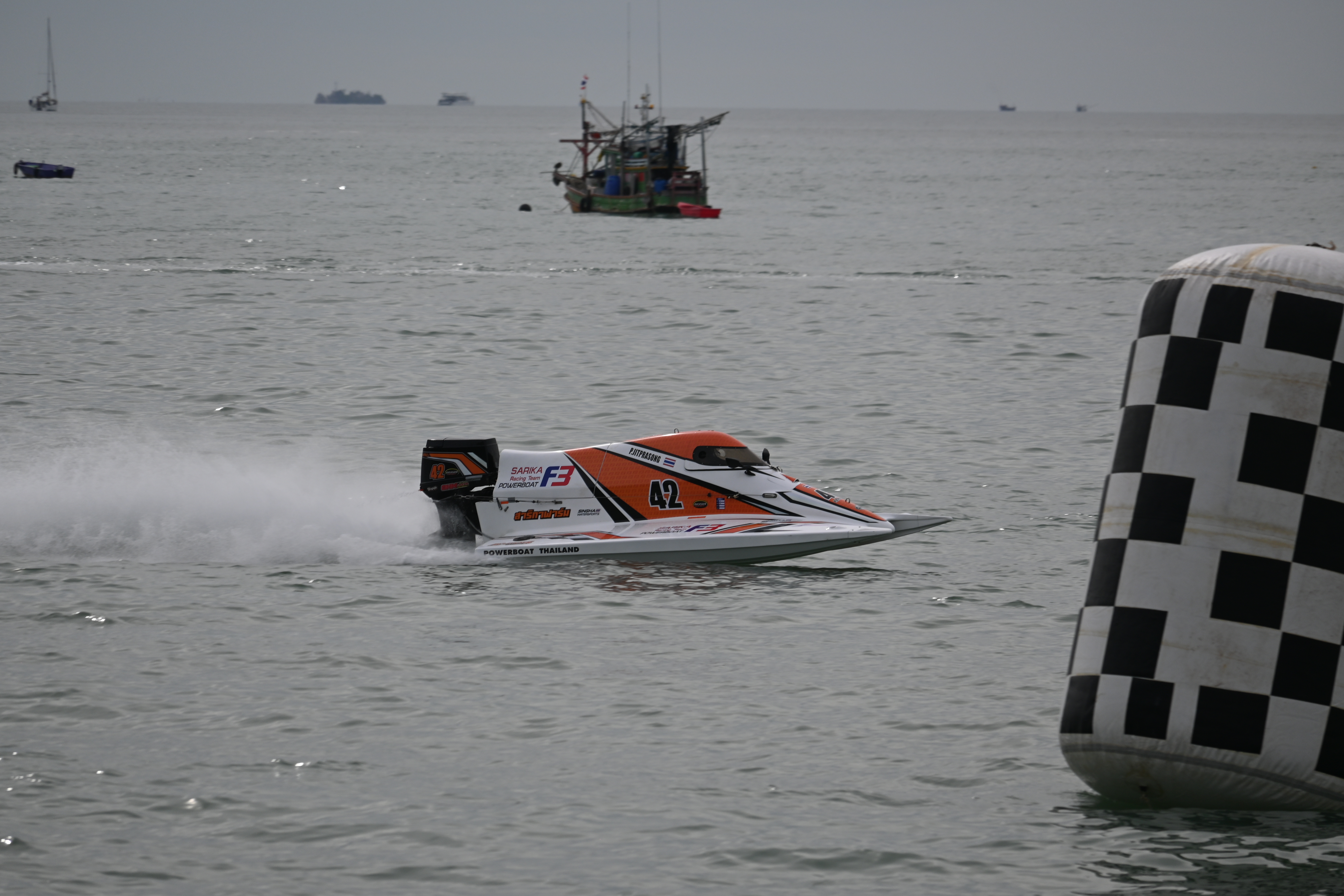 An orange and white racing powerboat speeds past a checkered buoy on open water.