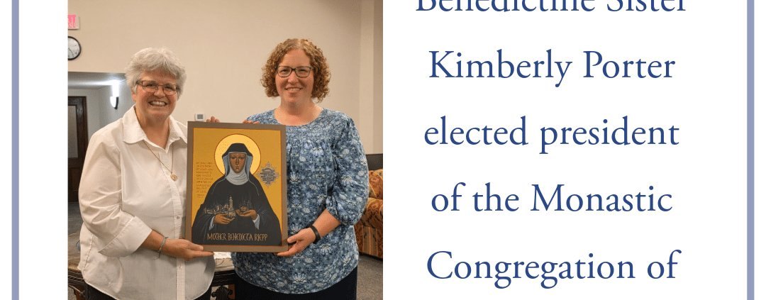 Two smiling women stand indoors, one presenting the other with a framed religious icon.