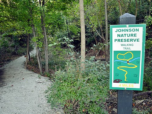 Sign and gravel path leading into a wooded nature preserve trail.