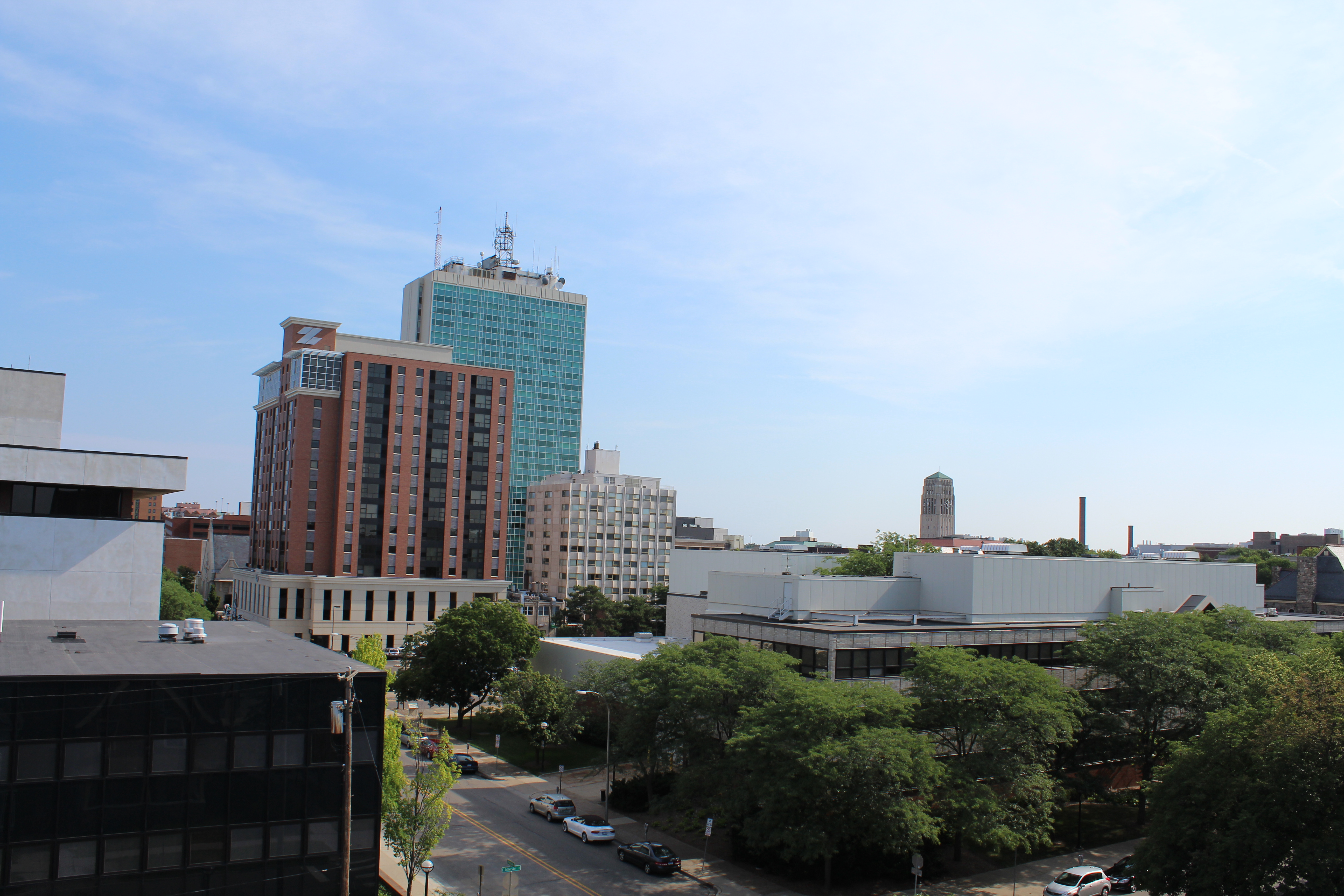 Downtown Ann Arbor skyline with multi-story buildings, trees, and a partly cloudy sky.
