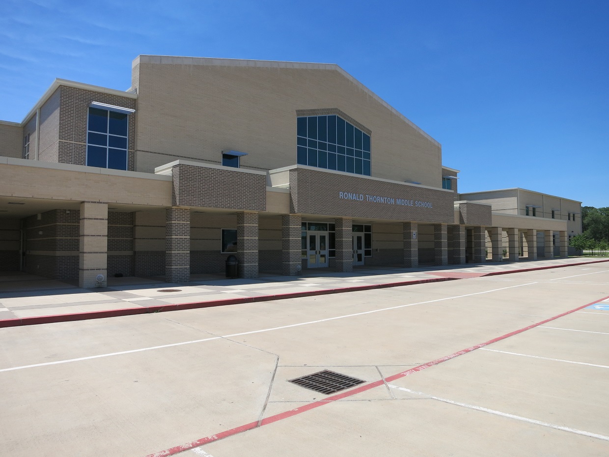 Large tan brick school building with blue-framed windows and a wide concrete plaza in front.