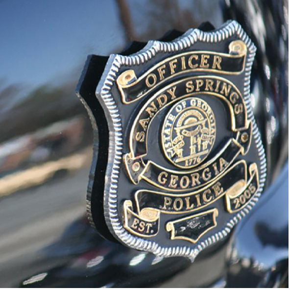 Gold and black Sandy Springs Police officer badge mounted on a dark surface.