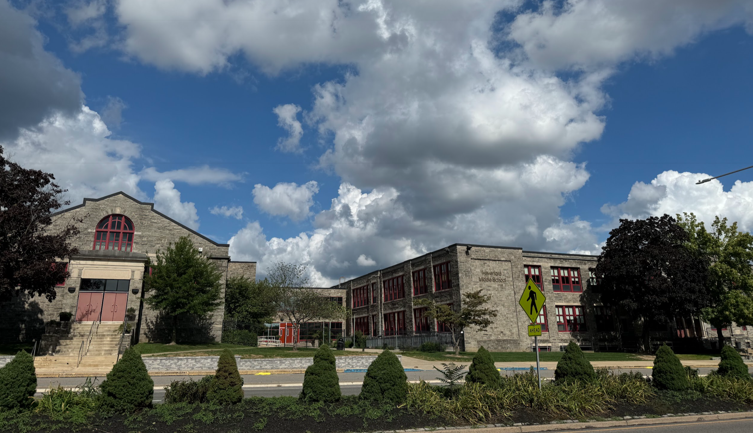 Large stone and brick school building with trimmed shrubs along the front facade.