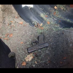 A black semi-automatic handgun lying on a dark ground surface near a tire.