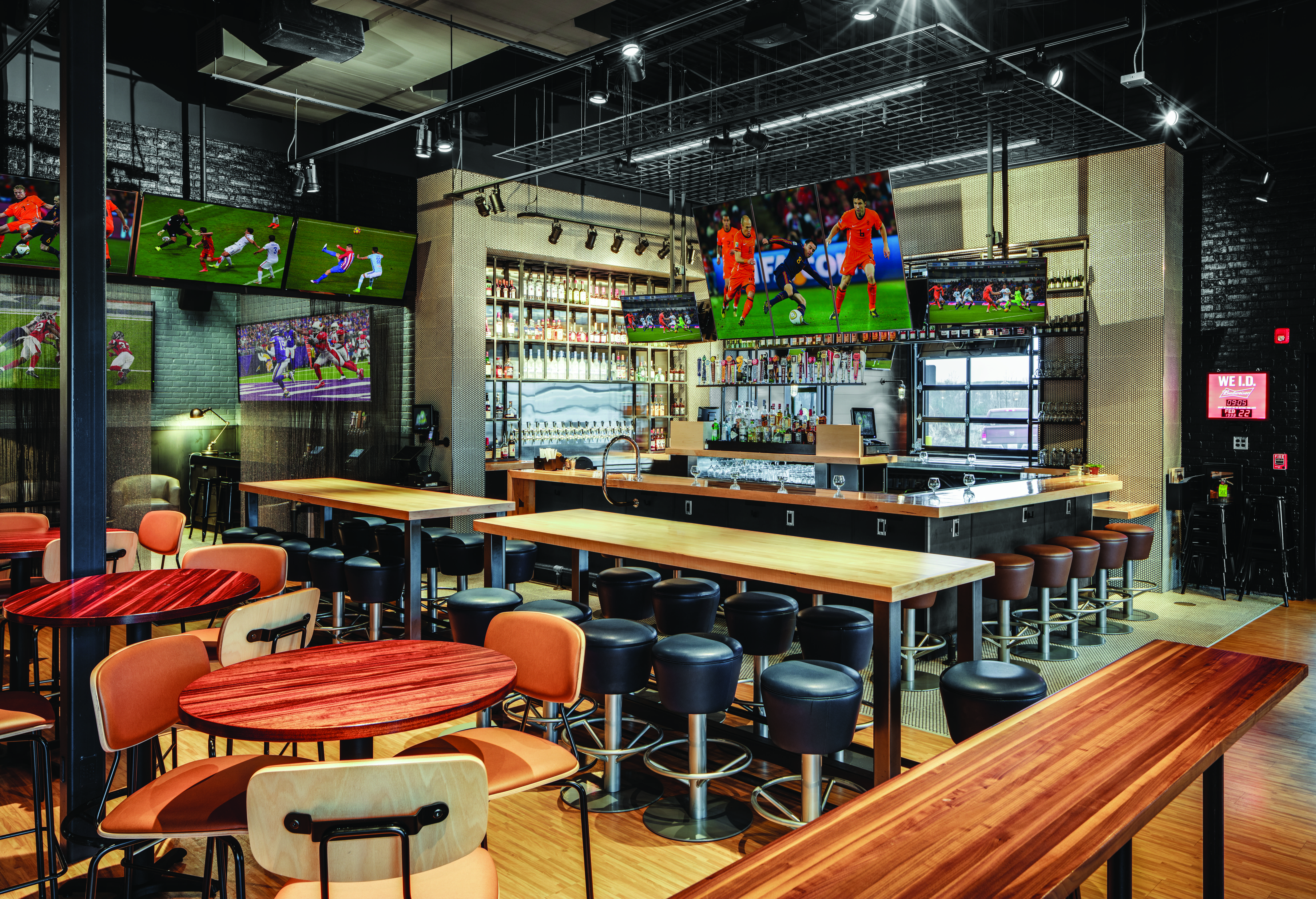 Sports bar interior with a central bar island, bar stools, and large TVs showing sports.