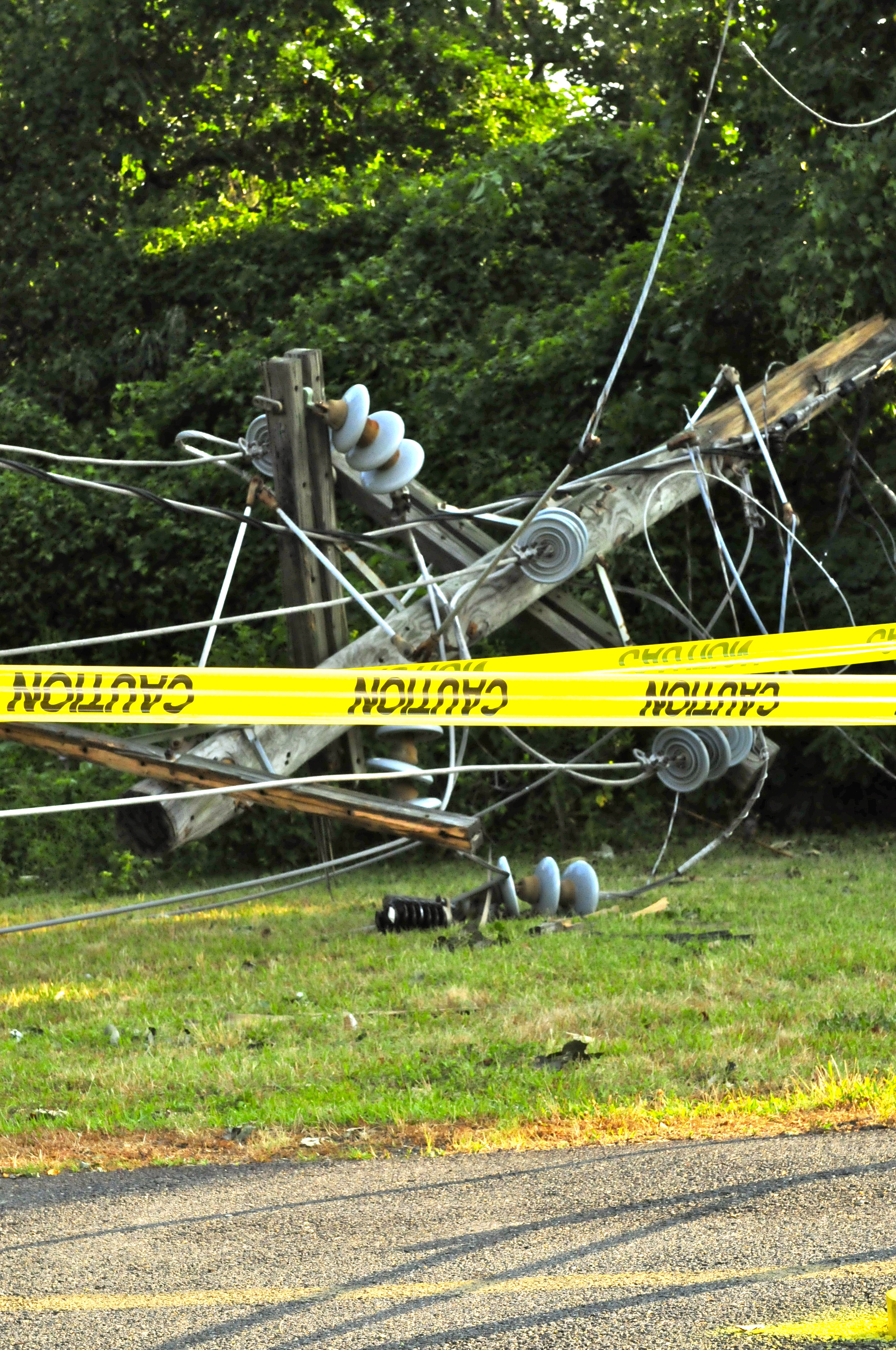 Collapsed utility pole with downed wires and caution tape on the ground.