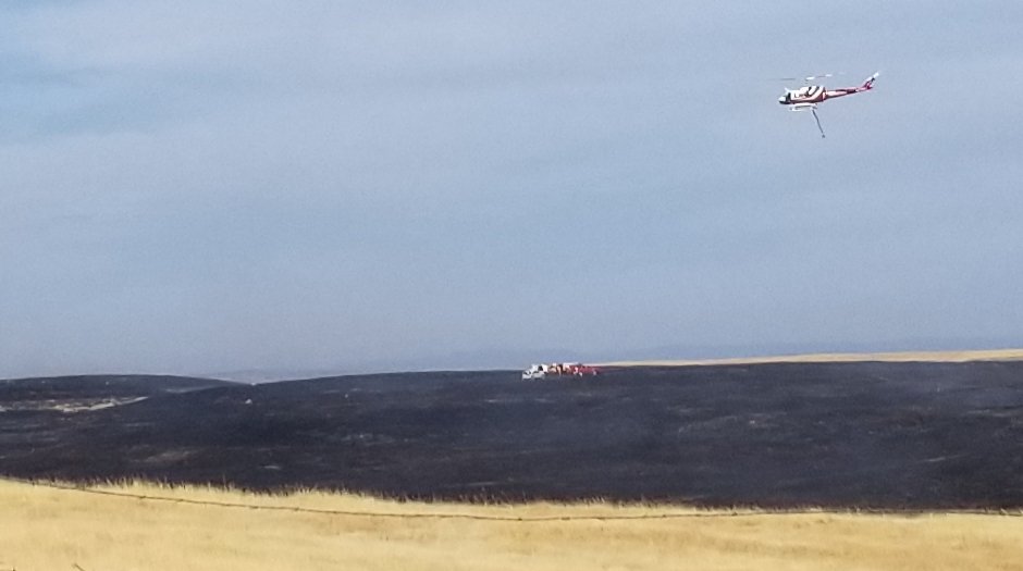 Aerial view of a grass fire burning across dry golden hillside with smoke rising