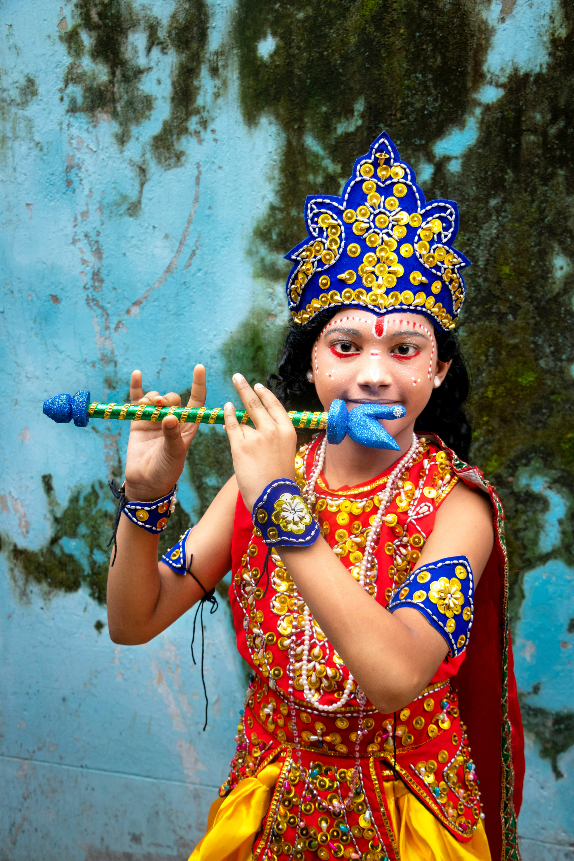 A child with blue face paint, gold crown, and decorated flute dressed as the Hindu deity Krishna.