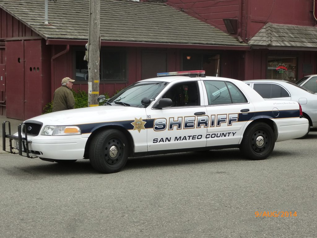 A white Ford Crown Victoria police cruiser marked 'SHERIFF San Mateo County' parked on a street.