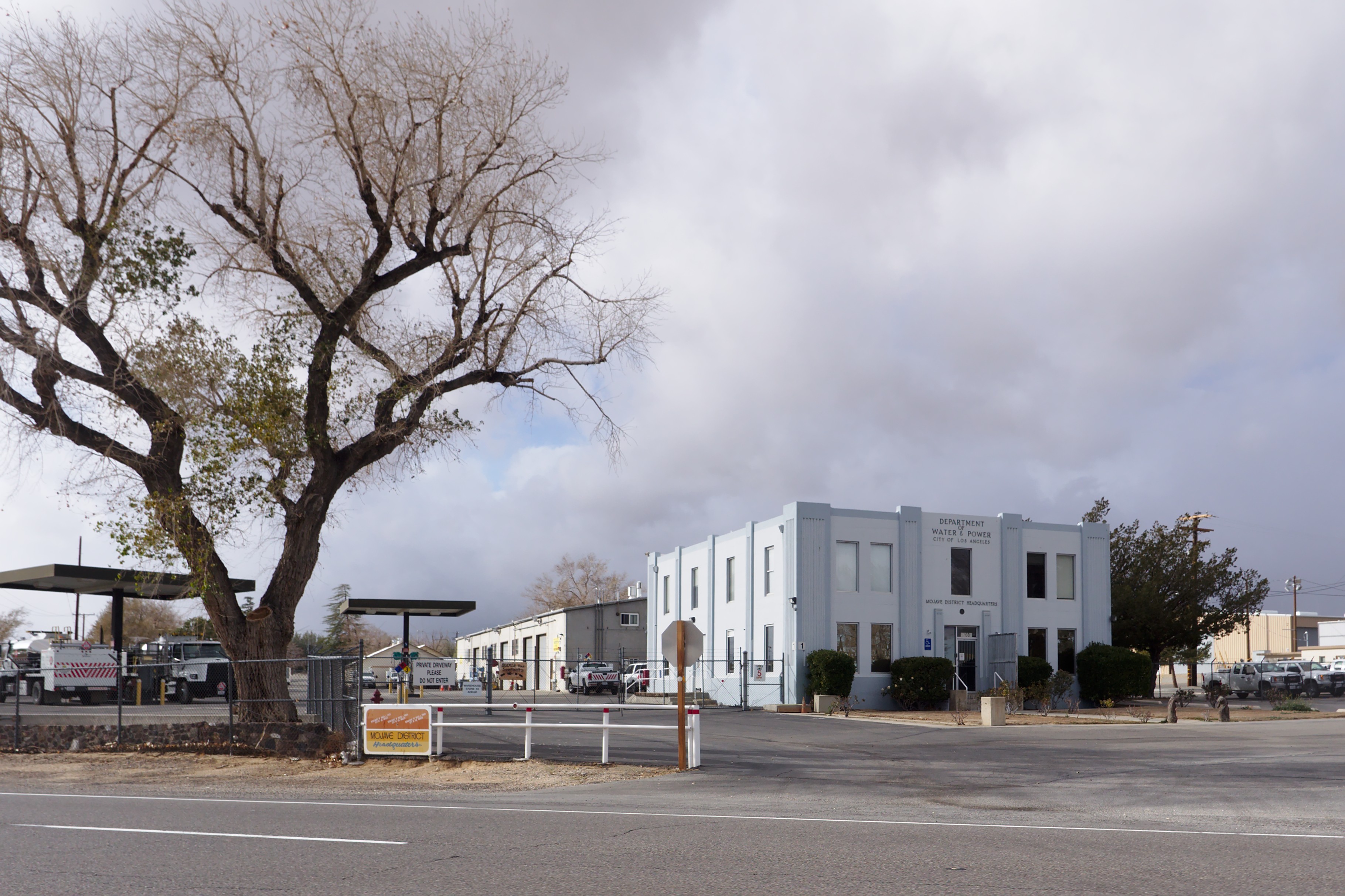 Two-story gray LADWP building with a bare tree in the foreground under an overcast sky.