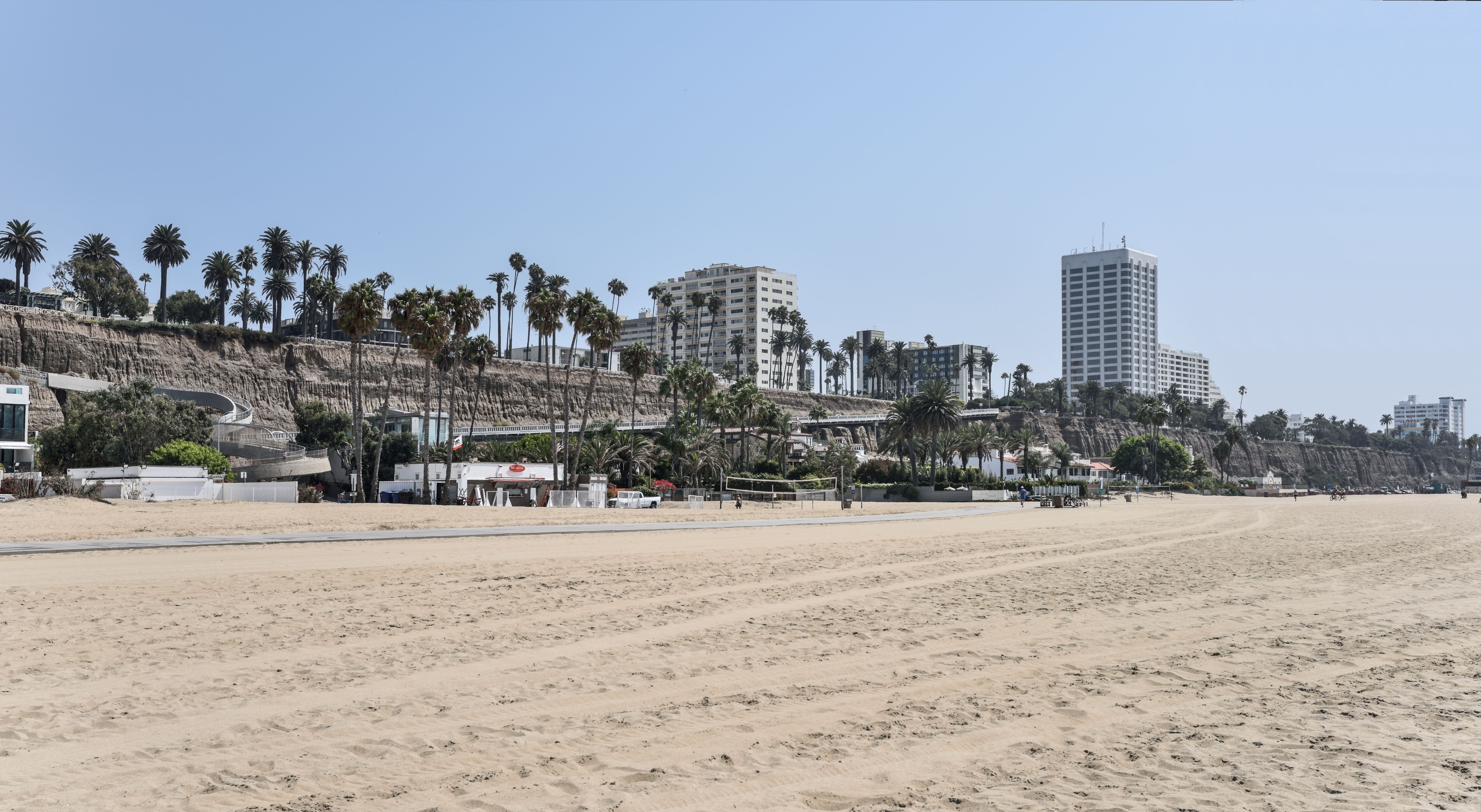Wide sandy beach below sandstone bluffs topped with palm trees and buildings.