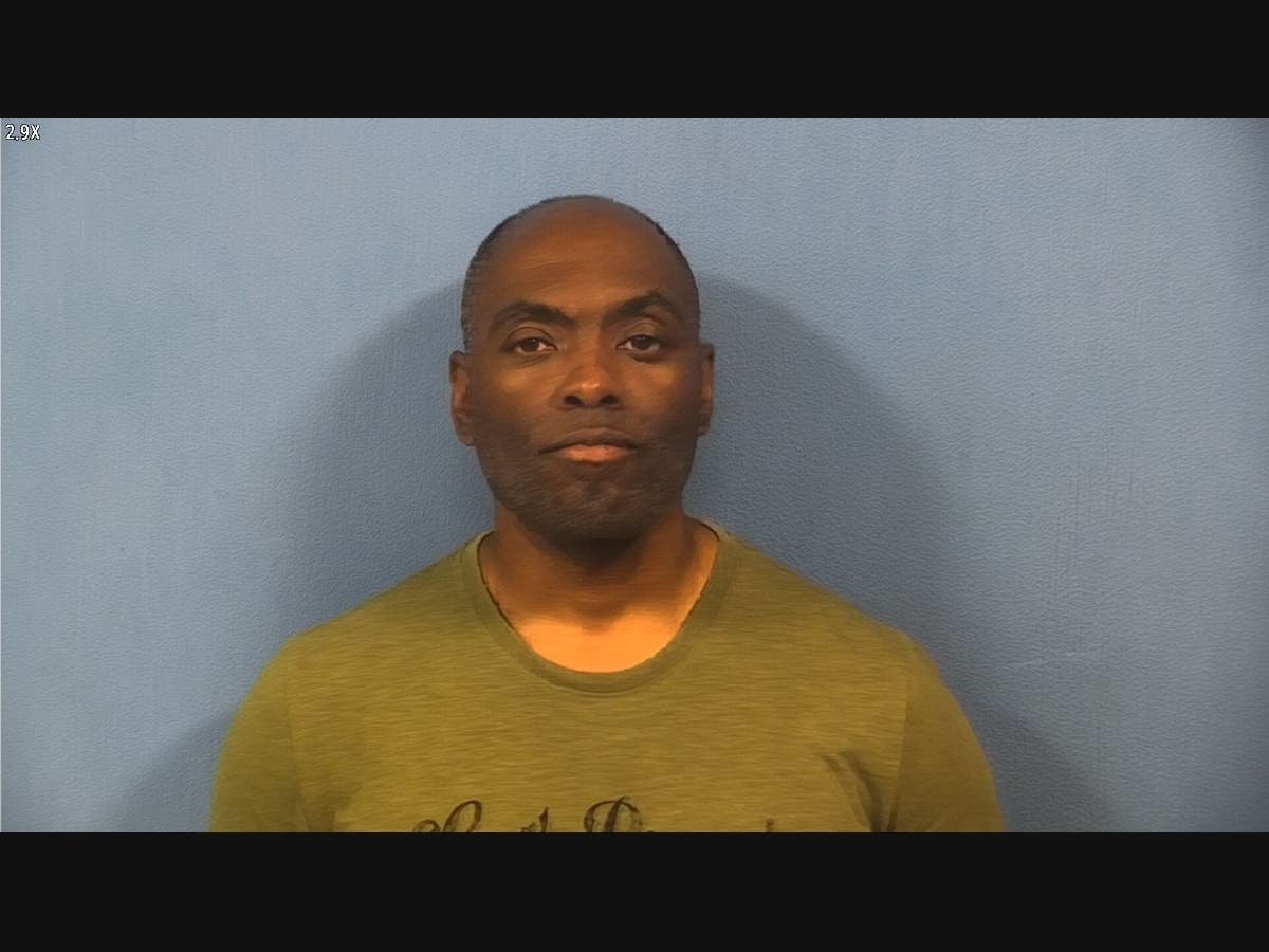 Booking photo of a middle-aged man in a green t-shirt against a light blue wall.