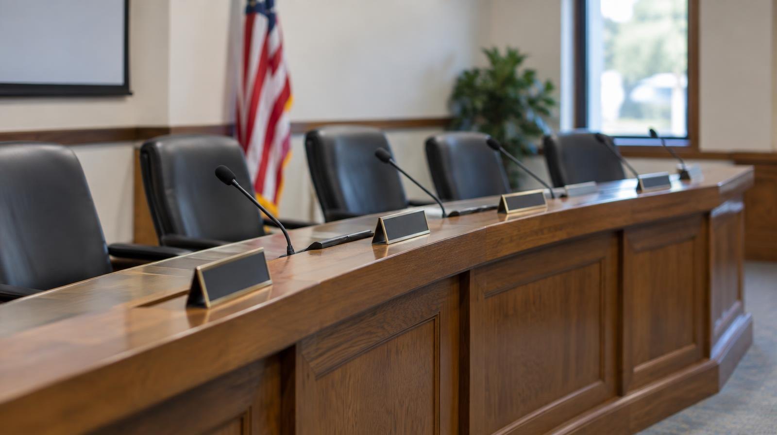 Empty curved wooden dais with name placards and microphones in a government chamber.