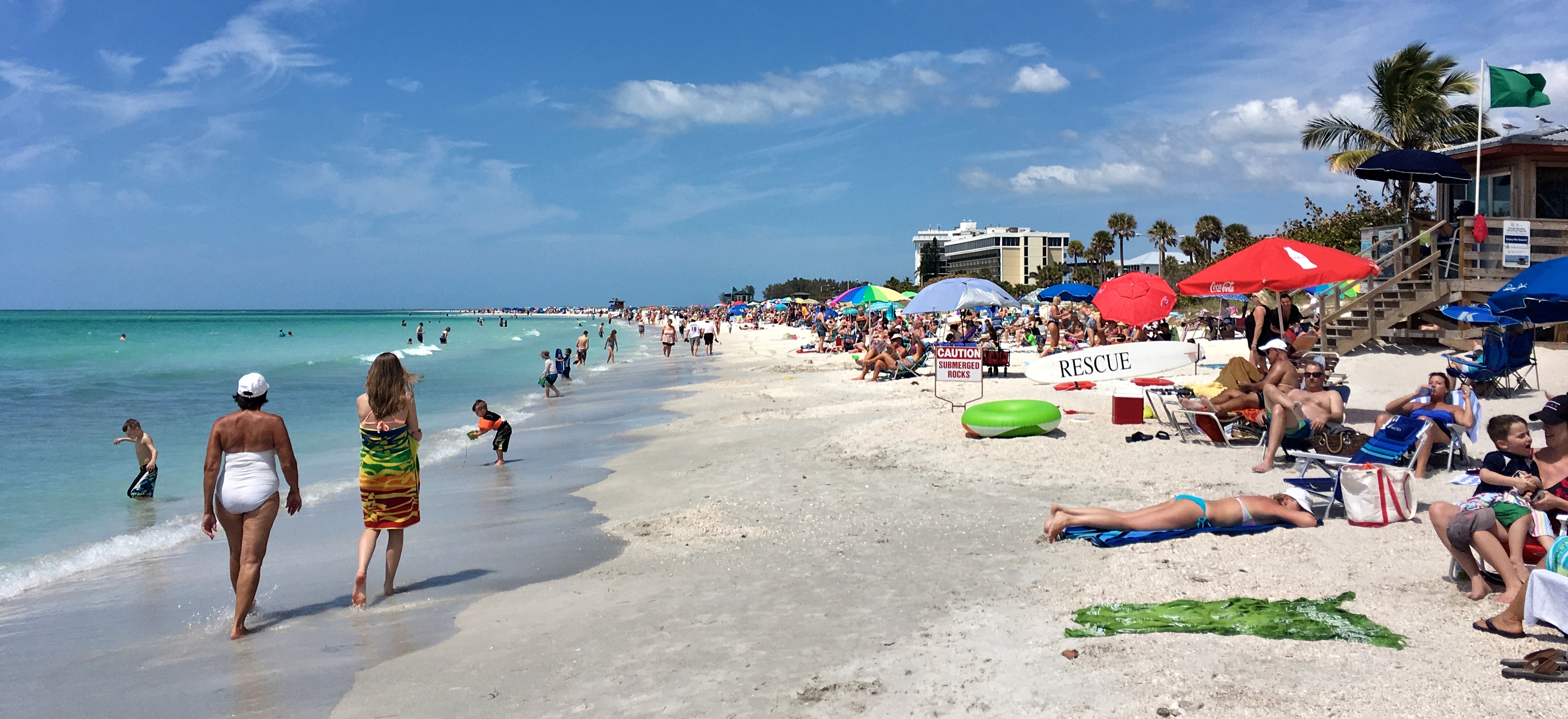 Crowded sandy beach with turquoise water, colorful umbrellas, and a lifeguard tower
