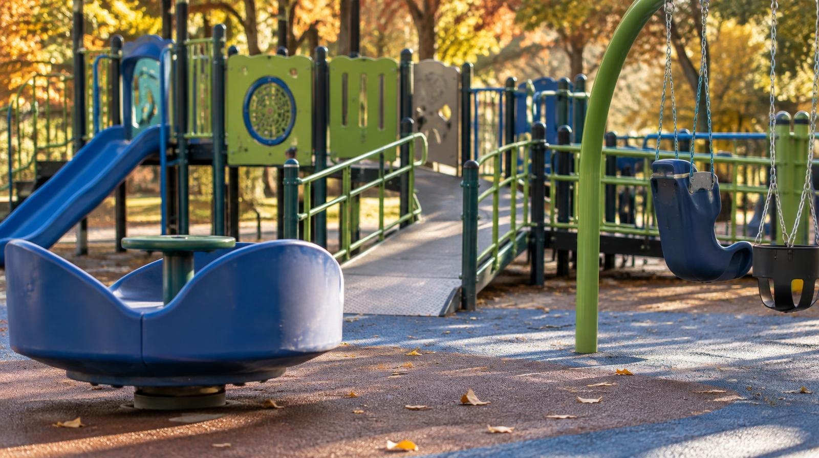 Colorful accessible playground structure with ramps, spinner, and swing seats on rubber surface.