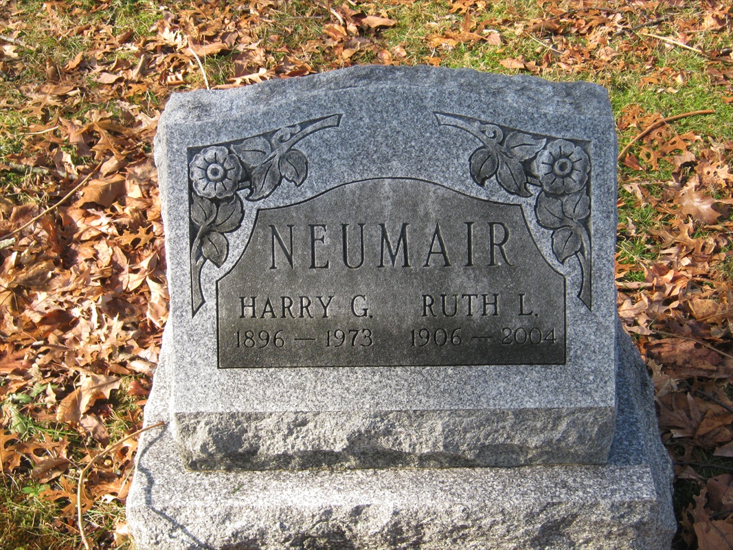 A gray granite headstone with two name panels surrounded by fallen autumn leaves.