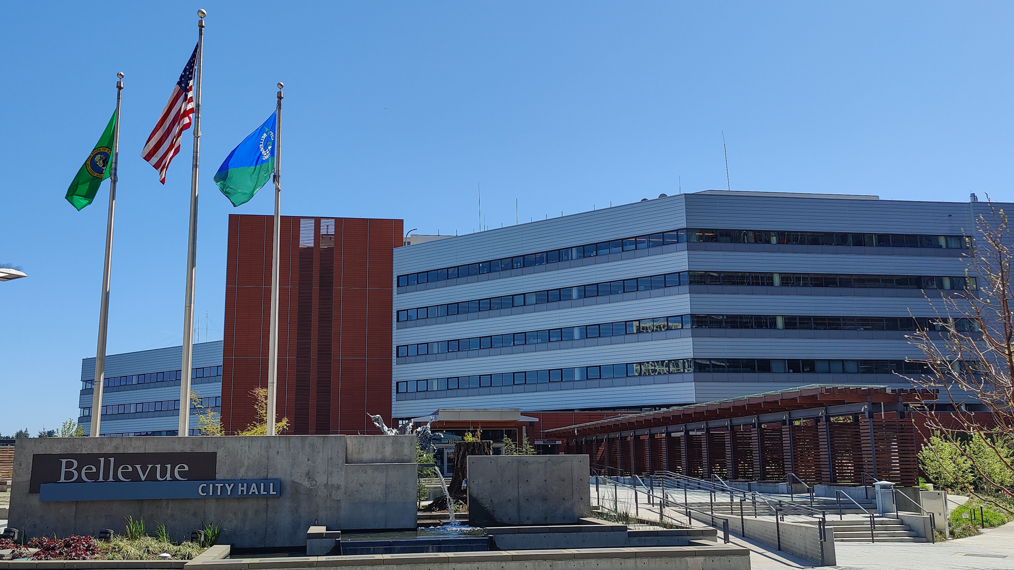 Exterior of Bellevue City Hall with three flags on flagpoles and a stone sign.