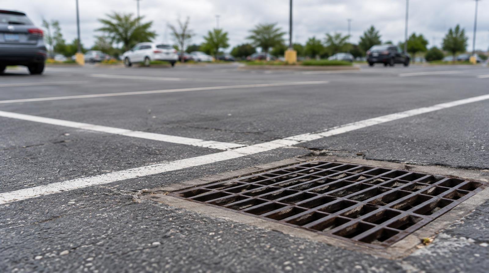 Asphalt parking lot with painted white lines and metal drainage grates in the pavement