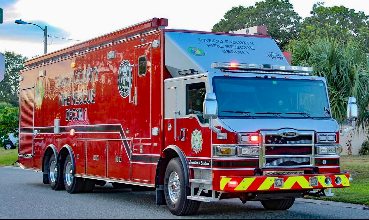 Large red Pasco County Fire Rescue emergency truck with lights on a street.