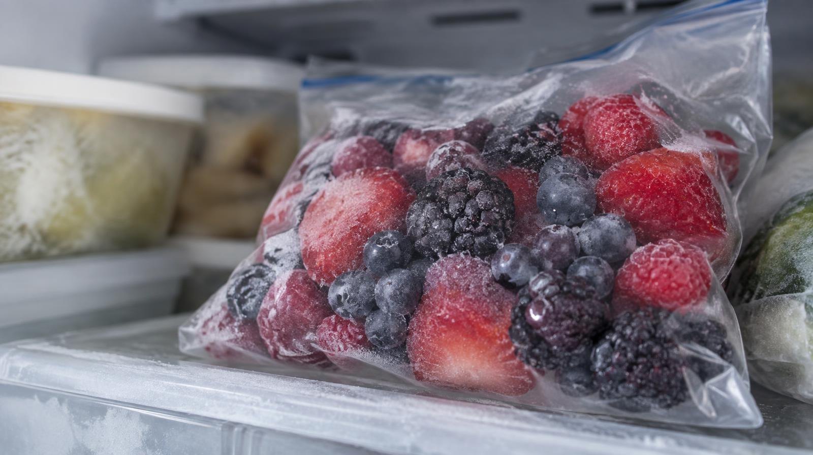 Clear plastic bag of frozen mixed berries on a frosted freezer shelf.