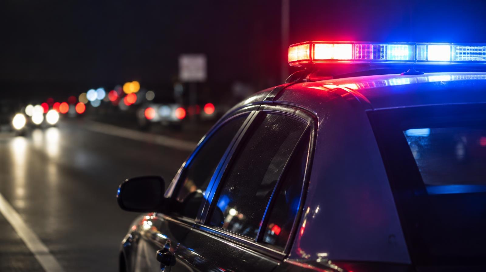 Red and blue police emergency lights glowing on a dark road at night.