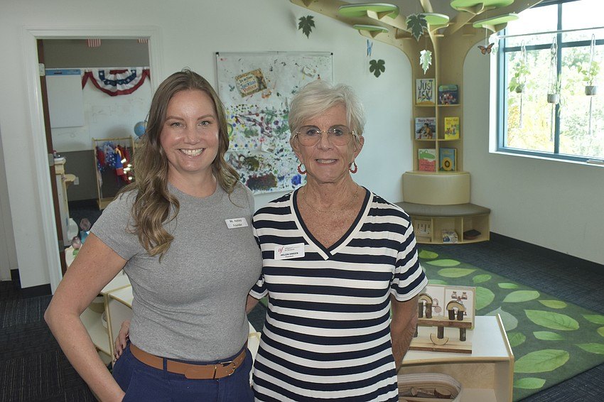 Two women smile together inside a colorful children's learning facility.
