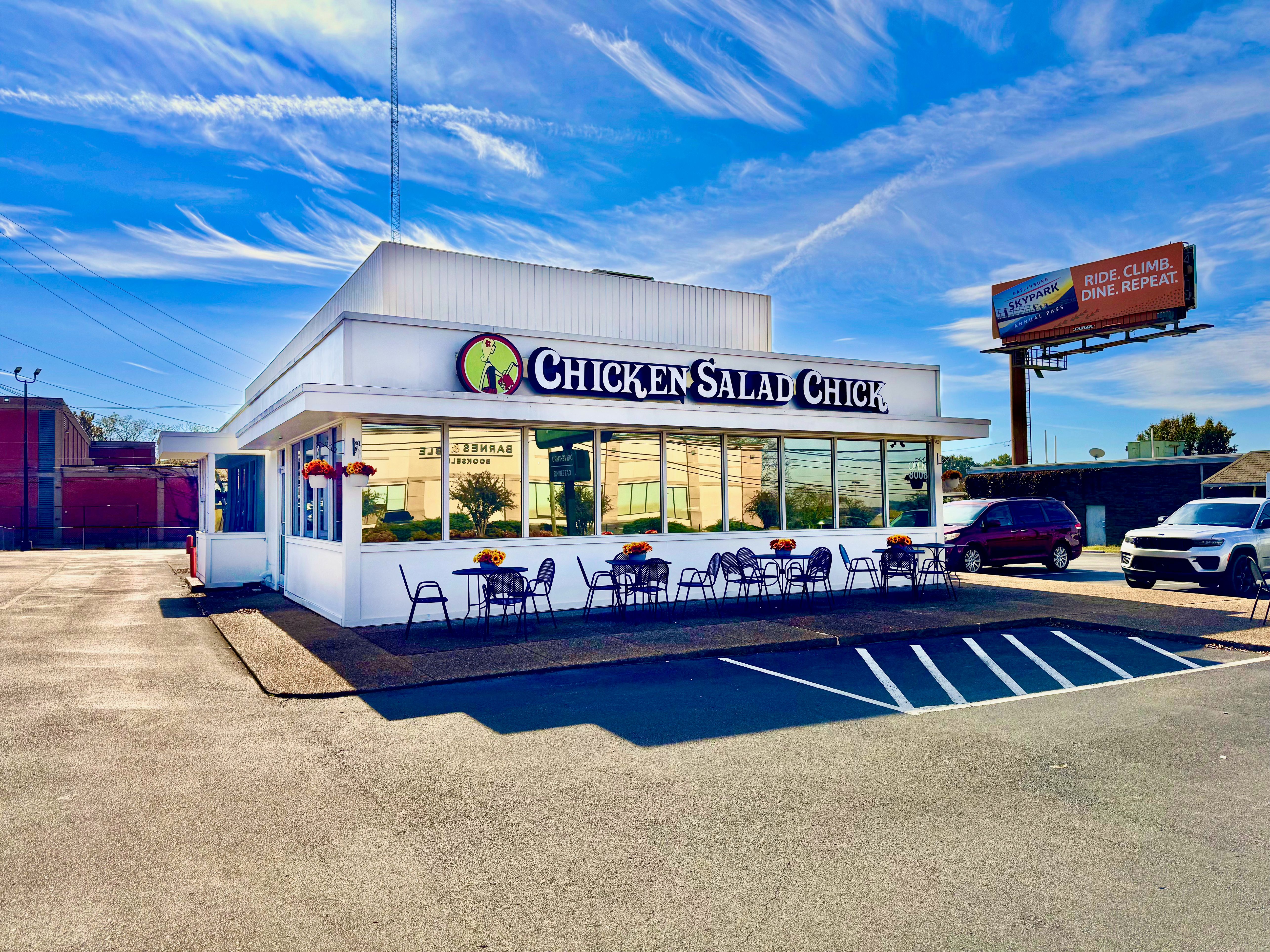 White Chicken Salad Chick restaurant building with outdoor seating and parking lot.