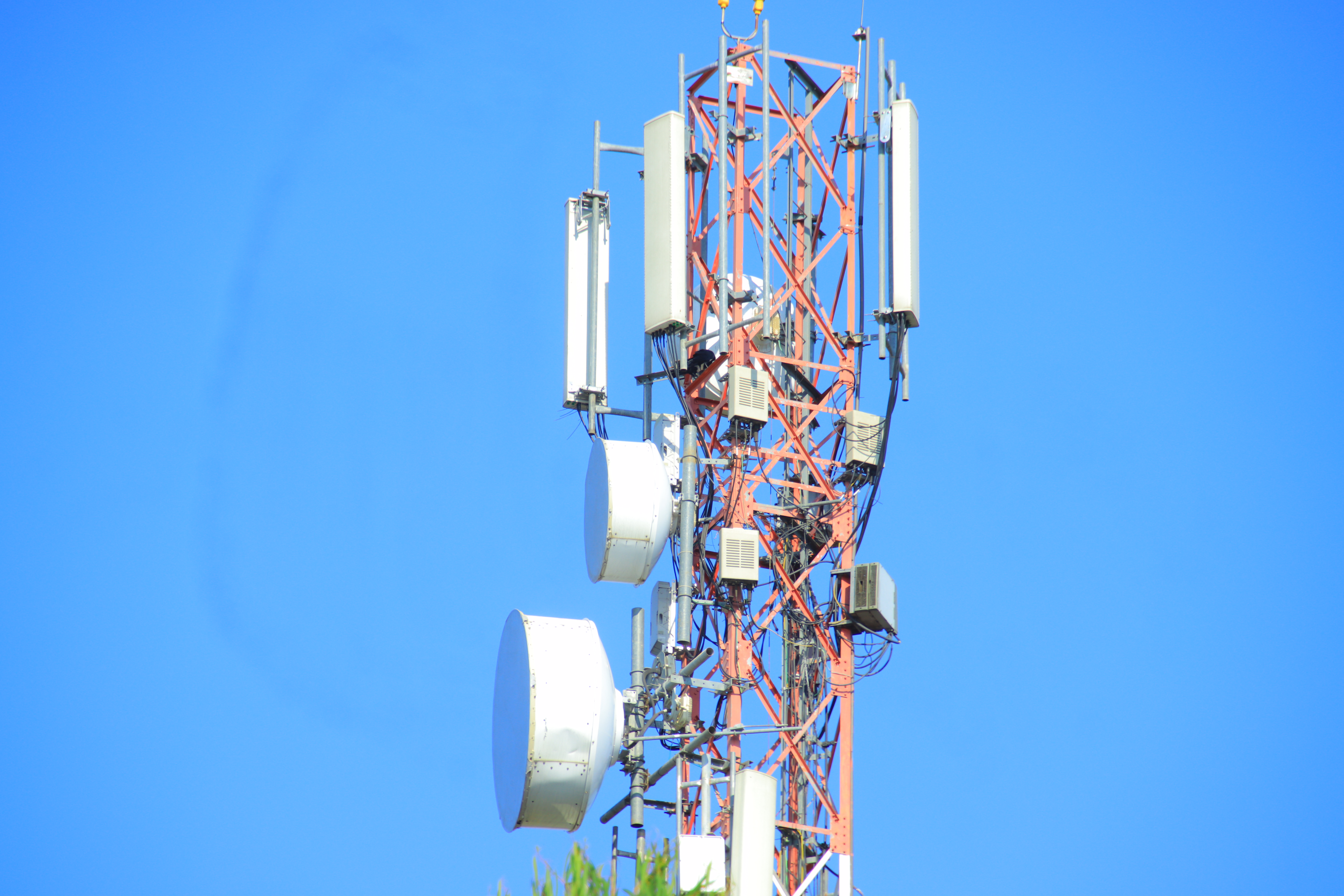 Red and white lattice cell tower with multiple panel antennas against a clear blue sky.
