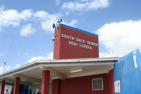 Front entrance of a red brick high school building with a sign above the door.