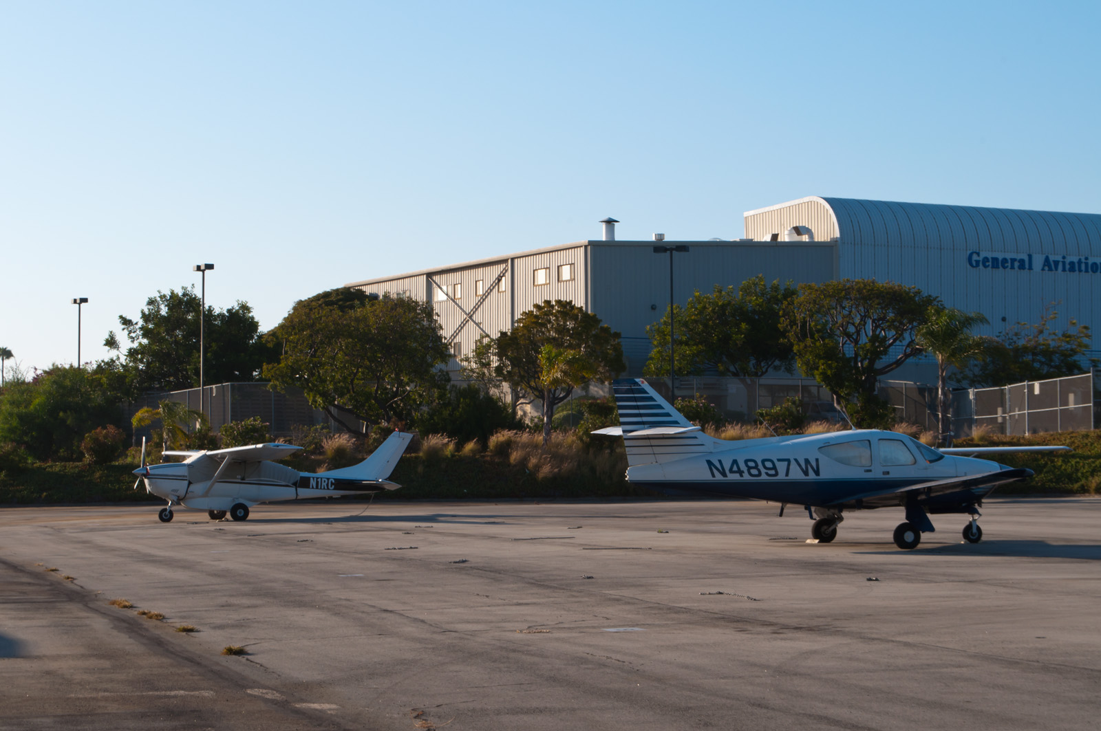 Two small propeller aircraft parked on a sunny airport tarmac apron.