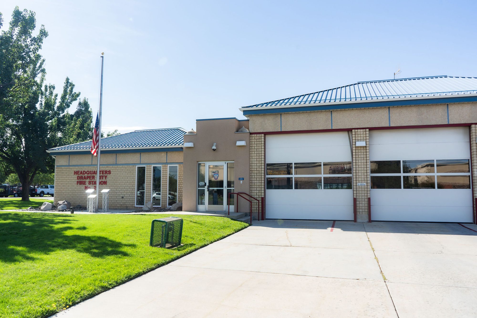 Single-story brick fire station with two garage bays and a flagpole out front.
