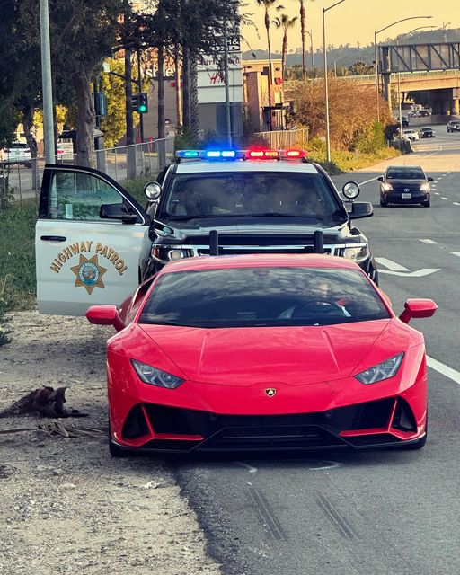 Police cruiser with lights on stopped behind a red sports car on a roadway.